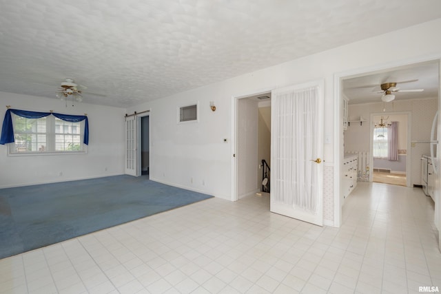 empty room with plenty of natural light, a barn door, and ceiling fan