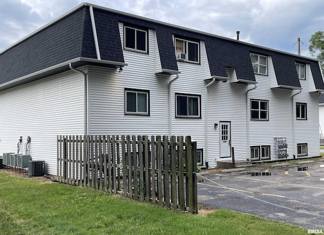 back of property featuring fence, a shingled roof, mansard roof, and central AC unit