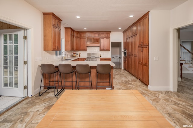 kitchen with a breakfast bar, kitchen peninsula, sink, decorative backsplash, and stainless steel range oven