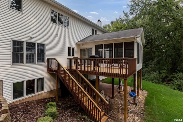 rear view of house featuring a wooden deck, a yard, and a sunroom