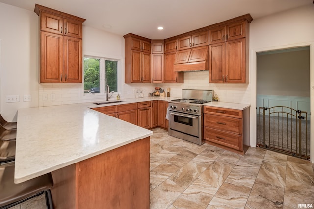 kitchen featuring high end stainless steel range oven, tasteful backsplash, kitchen peninsula, sink, and custom range hood