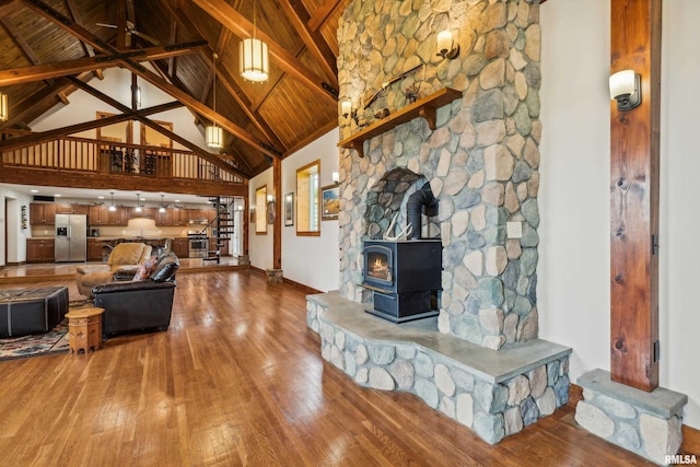 living room featuring beam ceiling, wood-type flooring, a wood stove, and high vaulted ceiling