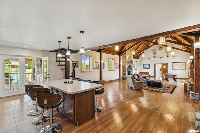 interior space featuring light hardwood / wood-style flooring, a breakfast bar, hanging light fixtures, vaulted ceiling with beams, and a center island