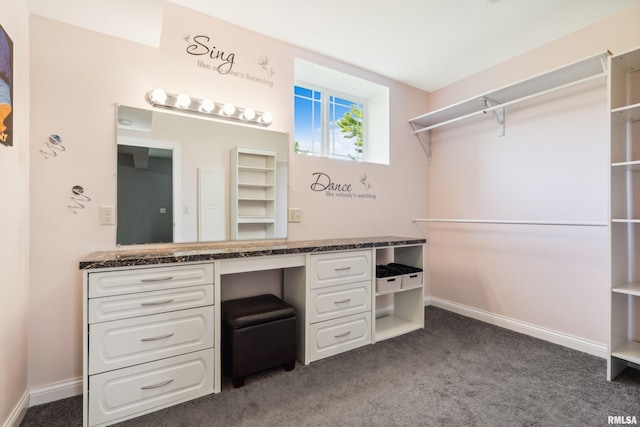 spacious closet with built in desk and dark colored carpet