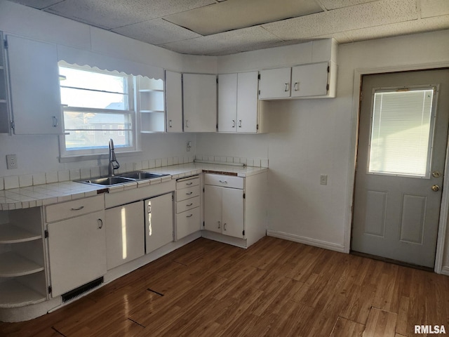 kitchen featuring a drop ceiling, sink, tile counters, and white cabinets