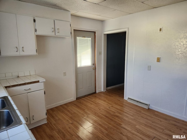 kitchen featuring sink, white cabinetry, tile countertops, light hardwood / wood-style floors, and a drop ceiling