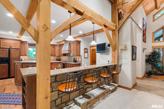 kitchen with light hardwood / wood-style flooring, tasteful backsplash, light stone counters, pendant lighting, and a kitchen bar