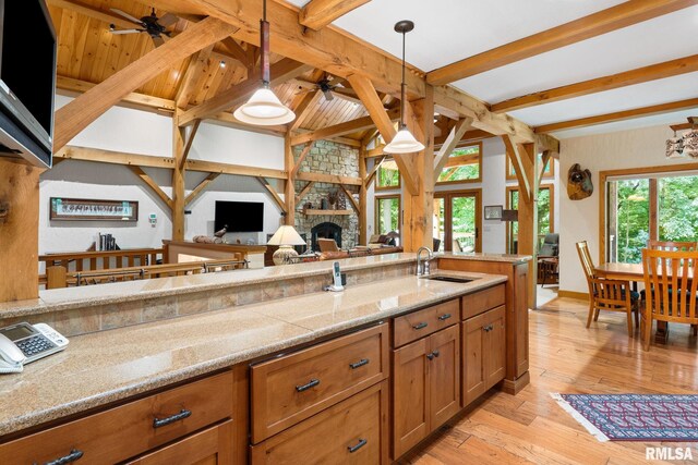 kitchen featuring ceiling fan, pendant lighting, beamed ceiling, light hardwood / wood-style flooring, and a stone fireplace