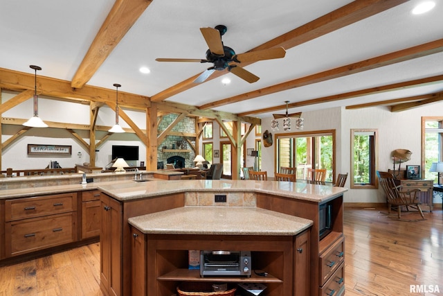 kitchen with beam ceiling, light wood-type flooring, a kitchen island, ceiling fan, and decorative light fixtures