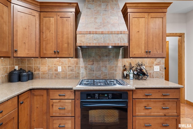 kitchen featuring premium range hood, oven, light stone counters, stainless steel gas cooktop, and backsplash