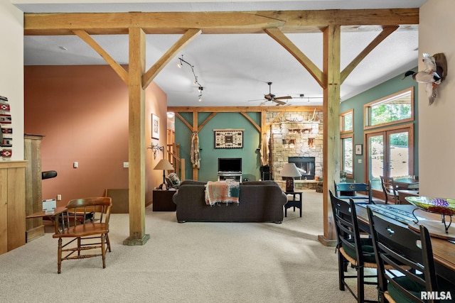 carpeted living room with a stone fireplace, french doors, rail lighting, beam ceiling, and ceiling fan