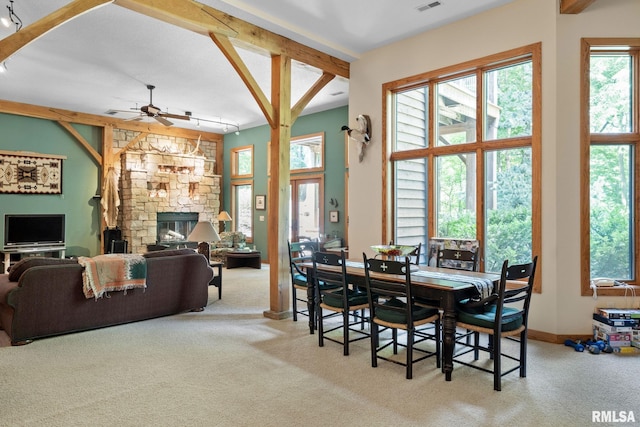 carpeted dining area featuring beamed ceiling, ceiling fan, a stone fireplace, and track lighting