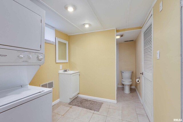 laundry area featuring stacked washer and clothes dryer, light tile patterned floors, and sink