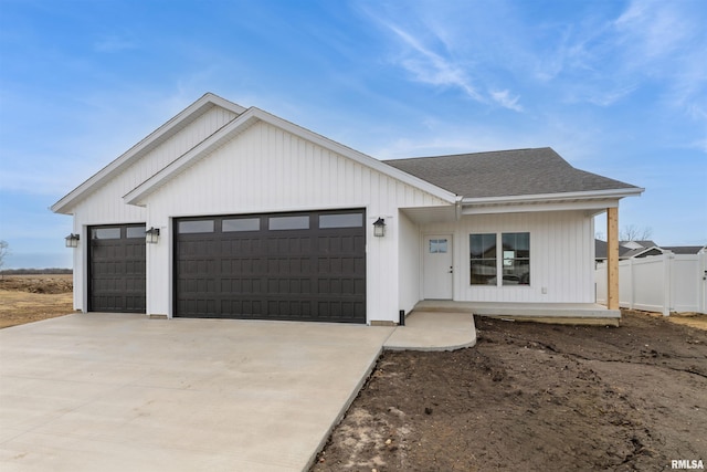 modern inspired farmhouse with fence, concrete driveway, an attached garage, and a shingled roof