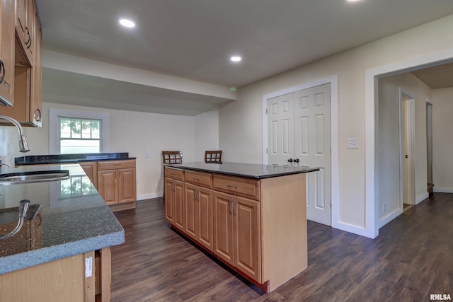 kitchen with sink, dark wood-type flooring, a kitchen island, and dark stone counters