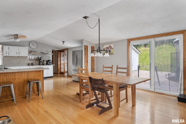 dining room with lofted ceiling, light wood finished floors, a textured ceiling, and a ceiling fan