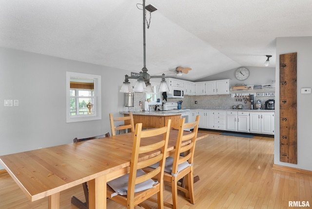 dining space featuring lofted ceiling, a textured ceiling, and light wood-style flooring