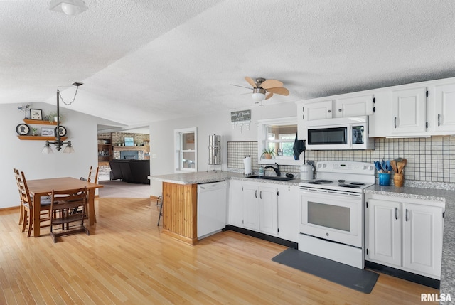 kitchen featuring light wood finished floors, white cabinetry, a sink, white appliances, and a peninsula