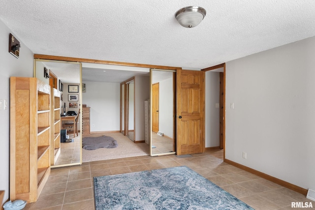 bedroom with a closet, a textured ceiling, baseboards, and tile patterned floors