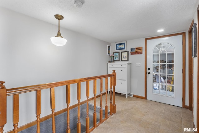 corridor featuring baseboards, a textured ceiling, and an upstairs landing