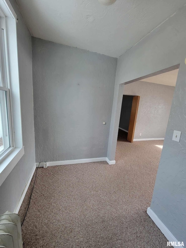 carpeted spare room with baseboards and a textured wall