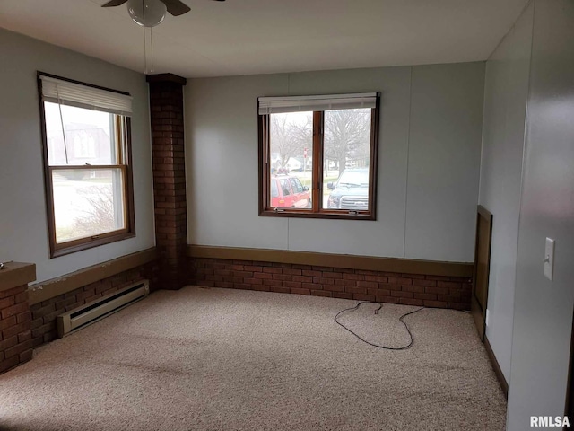 spare room with baseboard heating, carpet flooring, brick wall, and a ceiling fan