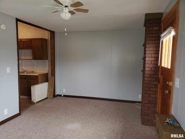 interior space with a ceiling fan, a sink, radiator heating unit, decorative columns, and baseboards