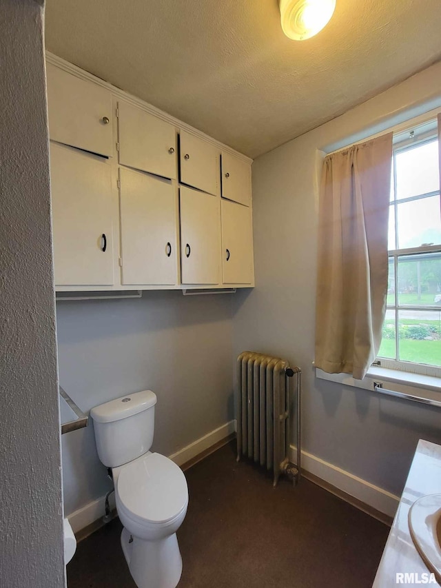 bathroom with baseboards, toilet, radiator heating unit, and a textured ceiling