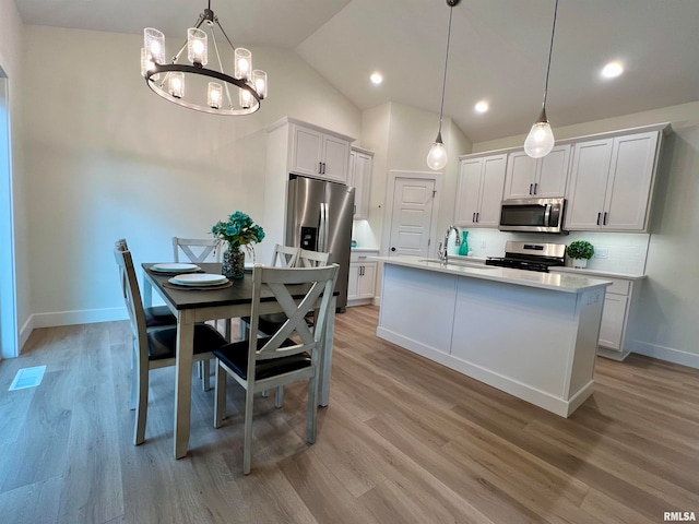 kitchen featuring light hardwood / wood-style floors, stainless steel appliances, hanging light fixtures, white cabinets, and an island with sink