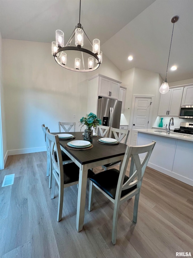 dining area with a notable chandelier, light hardwood / wood-style floors, sink, and vaulted ceiling