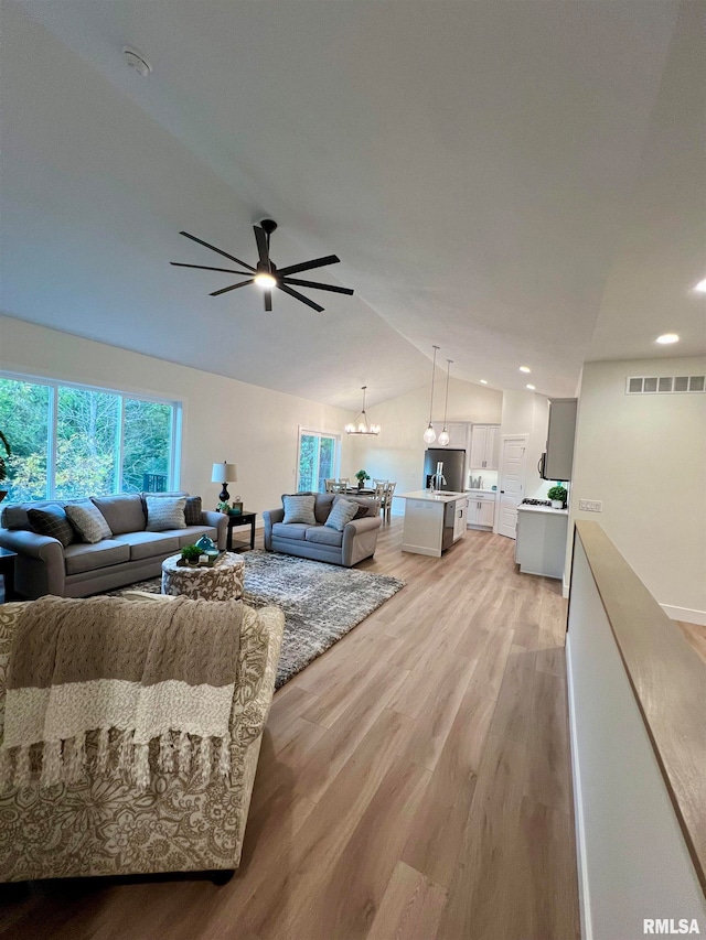 living room with ceiling fan with notable chandelier, light hardwood / wood-style floors, and vaulted ceiling