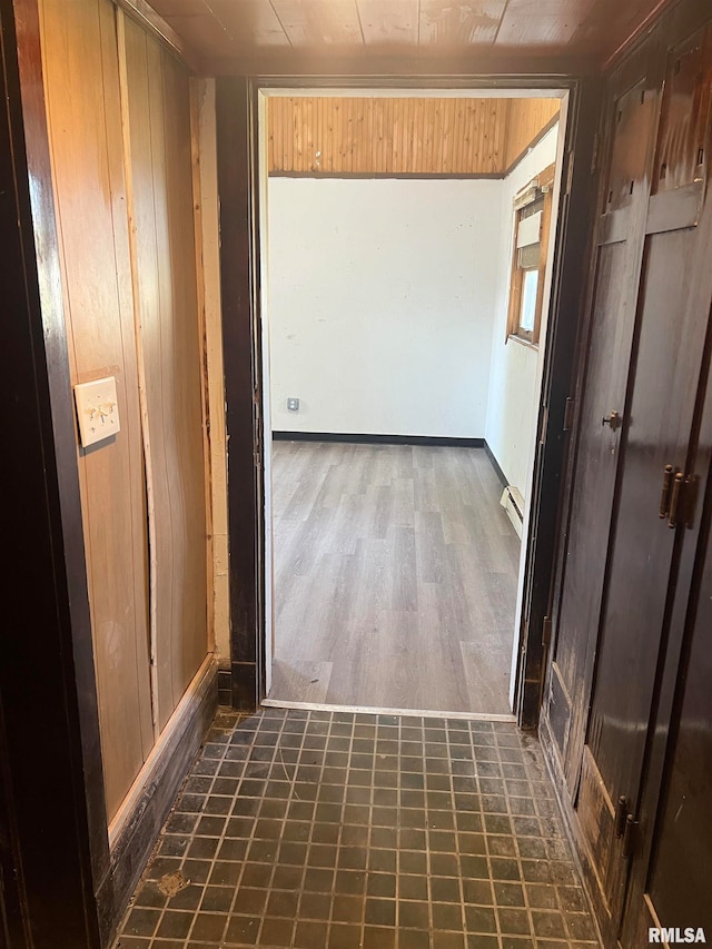 hallway with dark tile patterned flooring, baseboard heating, and wooden walls