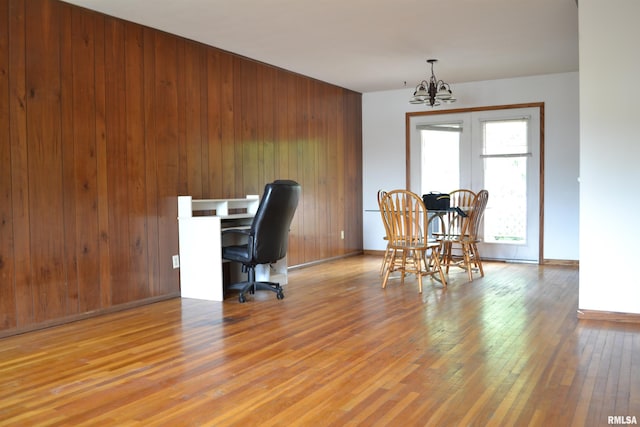 home office with a notable chandelier, wood walls, and hardwood / wood-style flooring