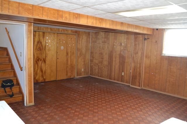 basement with a drop ceiling and wood walls