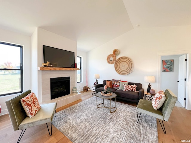 living room featuring vaulted ceiling, light wood finished floors, a tiled fireplace, and baseboards