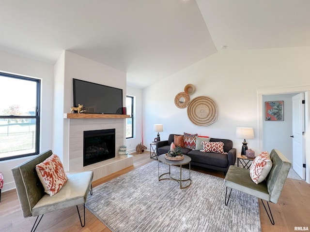 living room featuring vaulted ceiling, a tiled fireplace, light wood-type flooring, and baseboards