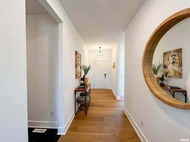 corridor with light wood-style floors, visible vents, and baseboards