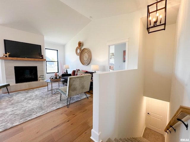 living area featuring vaulted ceiling, a tiled fireplace, wood finished floors, and a chandelier