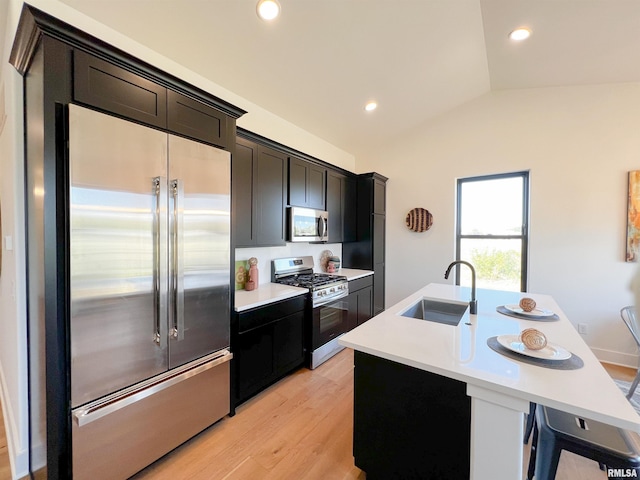 kitchen with a center island with sink, vaulted ceiling, stainless steel appliances, light countertops, and a sink