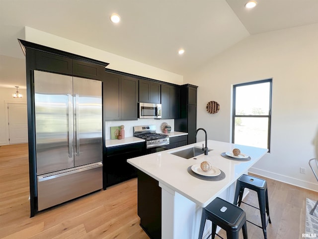 kitchen with stainless steel appliances, a sink, vaulted ceiling, light countertops, and a center island with sink