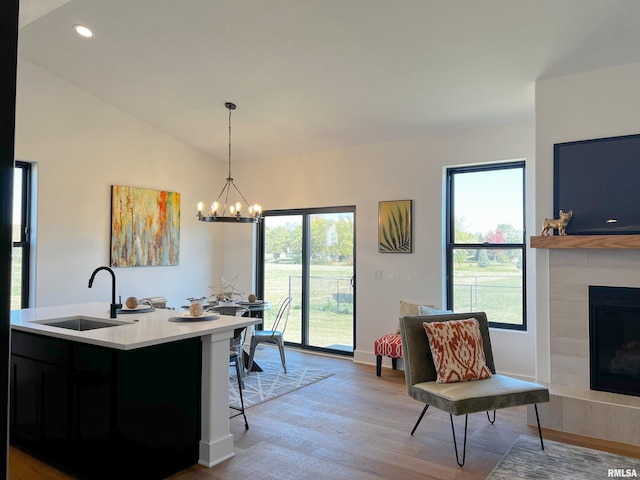 kitchen featuring a tiled fireplace, lofted ceiling, wood finished floors, light countertops, and a sink