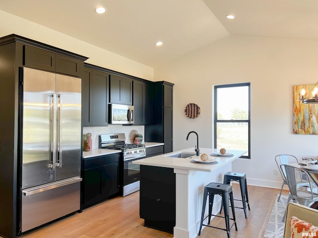 kitchen with lofted ceiling, light countertops, appliances with stainless steel finishes, a kitchen island with sink, and a sink