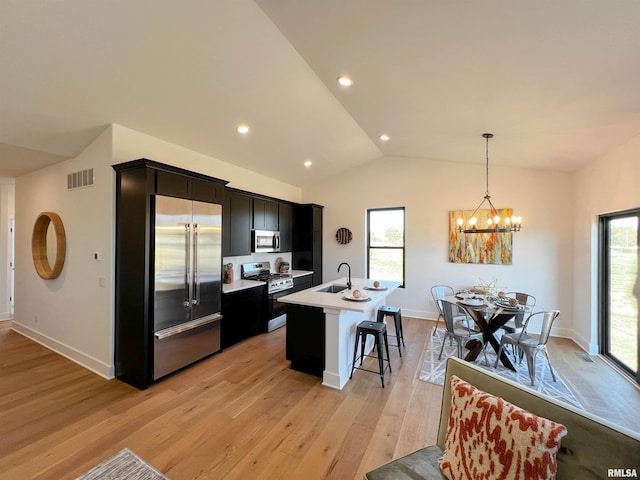 kitchen with visible vents, appliances with stainless steel finishes, light wood-style floors, a kitchen island with sink, and vaulted ceiling