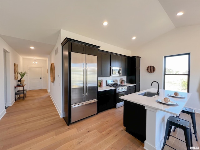 kitchen with lofted ceiling, a kitchen island with sink, stainless steel appliances, light countertops, and a sink