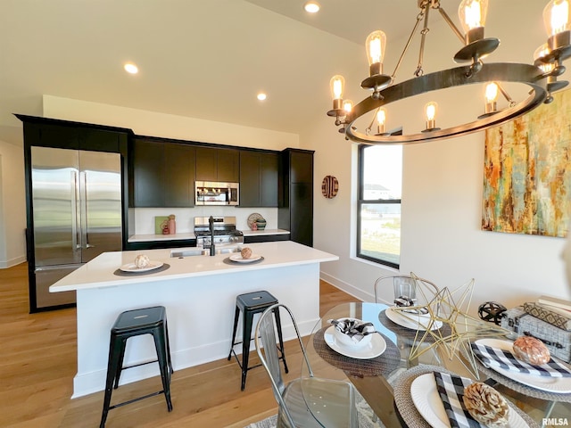 kitchen featuring light countertops, hanging light fixtures, appliances with stainless steel finishes, light wood-style floors, and an island with sink