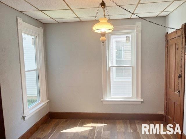 unfurnished dining area with a paneled ceiling, a wealth of natural light, and dark wood-type flooring