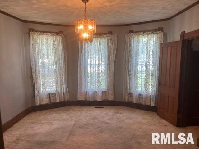 unfurnished dining area featuring carpet, ornamental molding, a textured ceiling, and an inviting chandelier