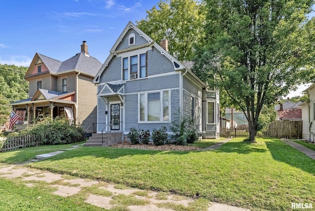 victorian-style house featuring a chimney, a front lawn, and fence