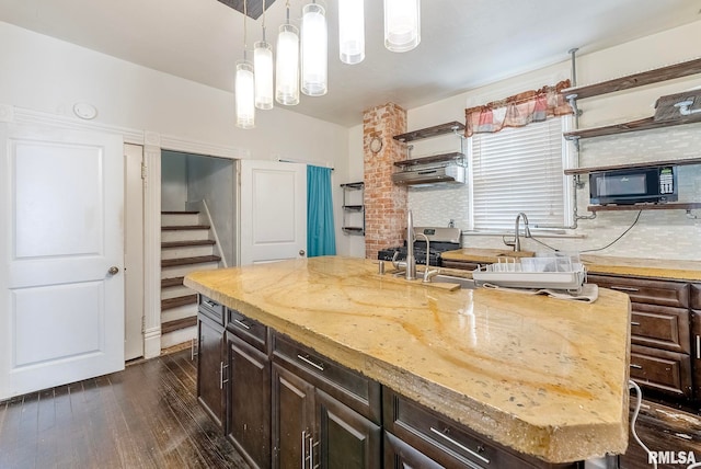 kitchen featuring open shelves, dark wood-type flooring, dark brown cabinets, and a center island with sink