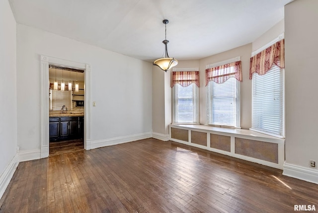 unfurnished dining area with a sink, baseboards, and dark wood-type flooring